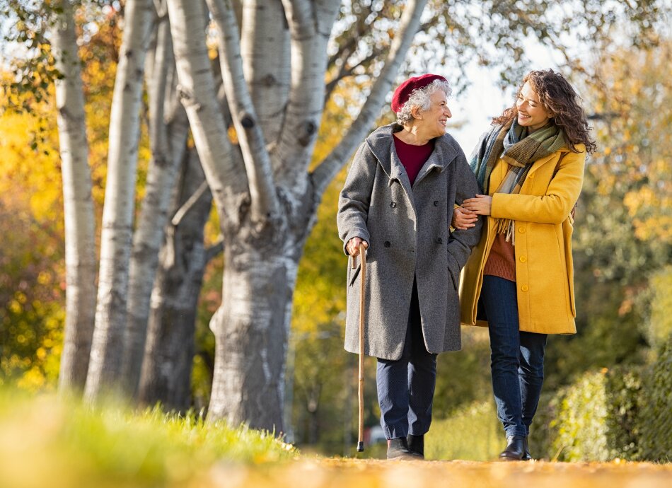 Woman helping older woman with walking stick outdoors